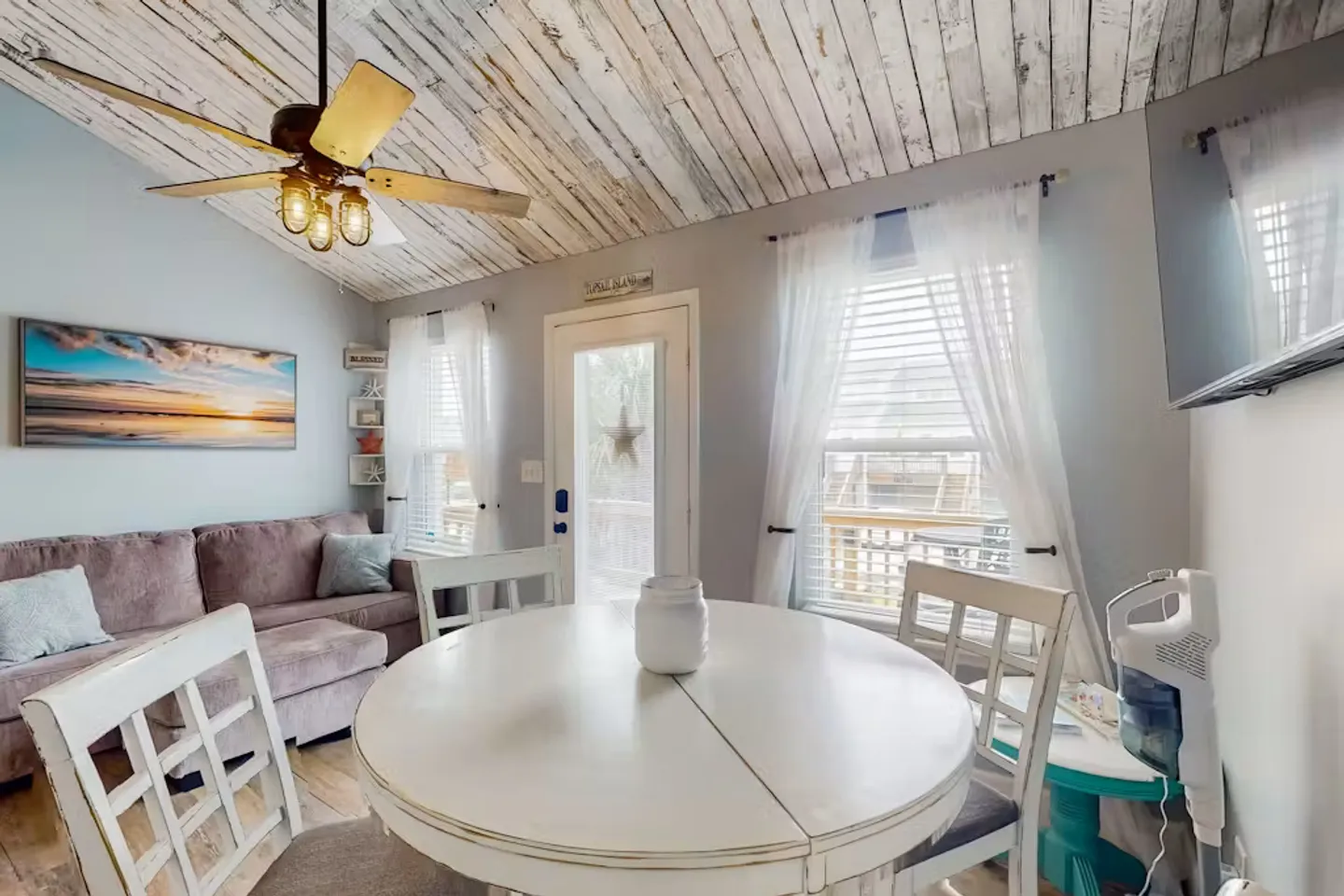 Dining area with a round white table and chairs in an open living space featuring a distressed wood plank ceiling and a ceiling fan.