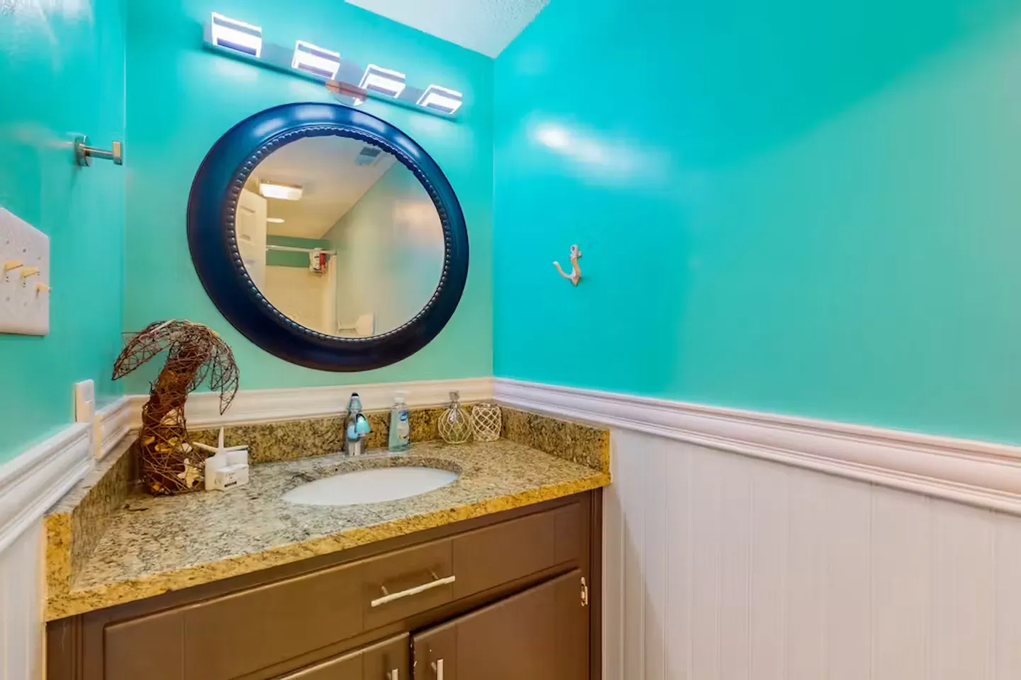 Bathroom vanity with a round mirror, bright turquoise walls, and white wainscoting.