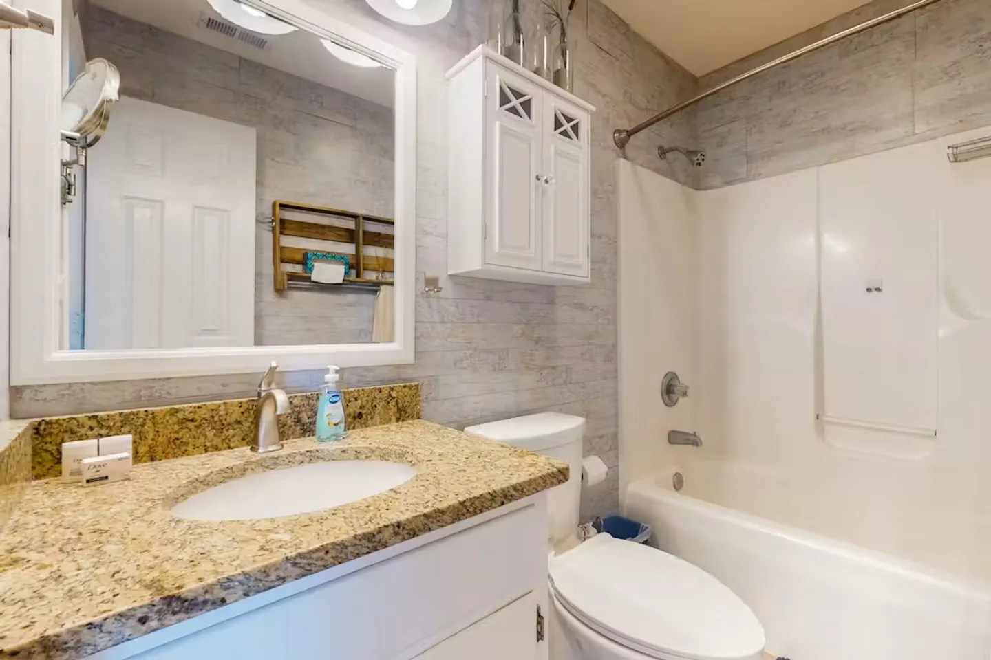 Bathroom featuring a vanity with speckled countertop, framed mirror, toilet, and combination bathtub and shower.