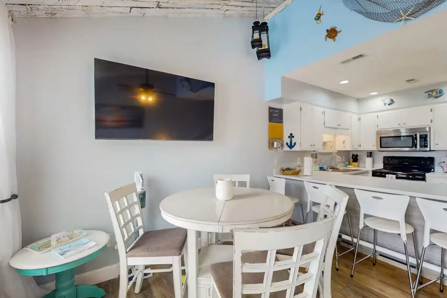 Dining area with a round white table and chairs next to an open kitchen with a breakfast counter.