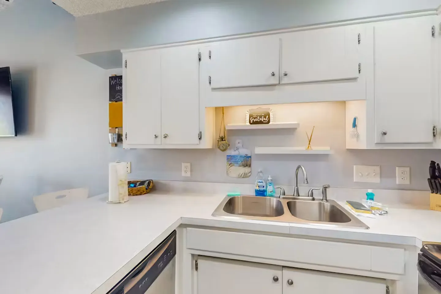 Kitchen counter and double sink with white painted cabinets and small floating shelves.
