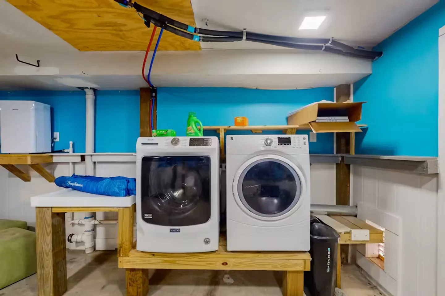 Front-loading washer and dryer sitting on a raised wooden platform in a basement laundry area with blue walls.