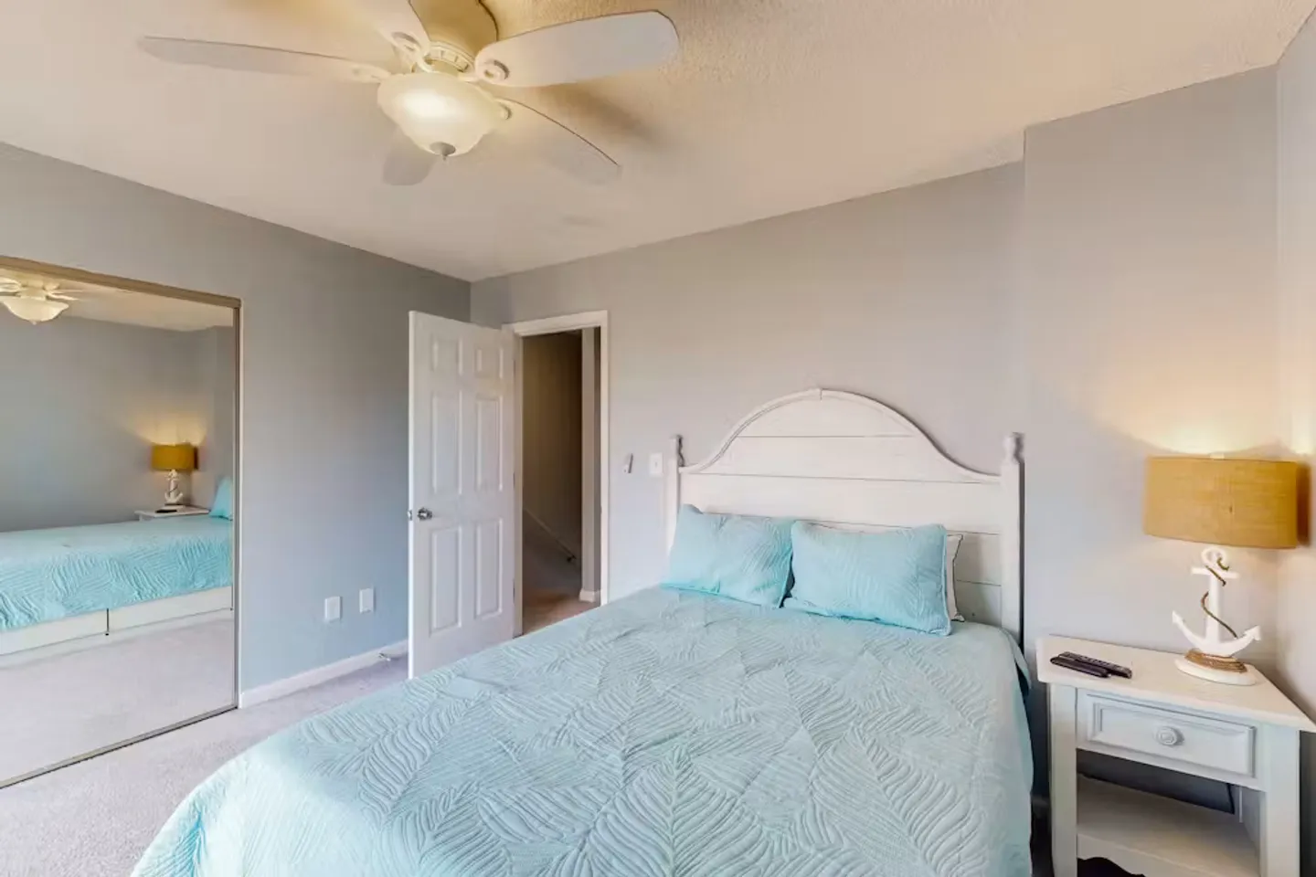 Bedroom featuring a bed with a light blue textured quilt, a white headboard, a matching nightstand with an anchor-themed lamp, and a large mirrored closet door.