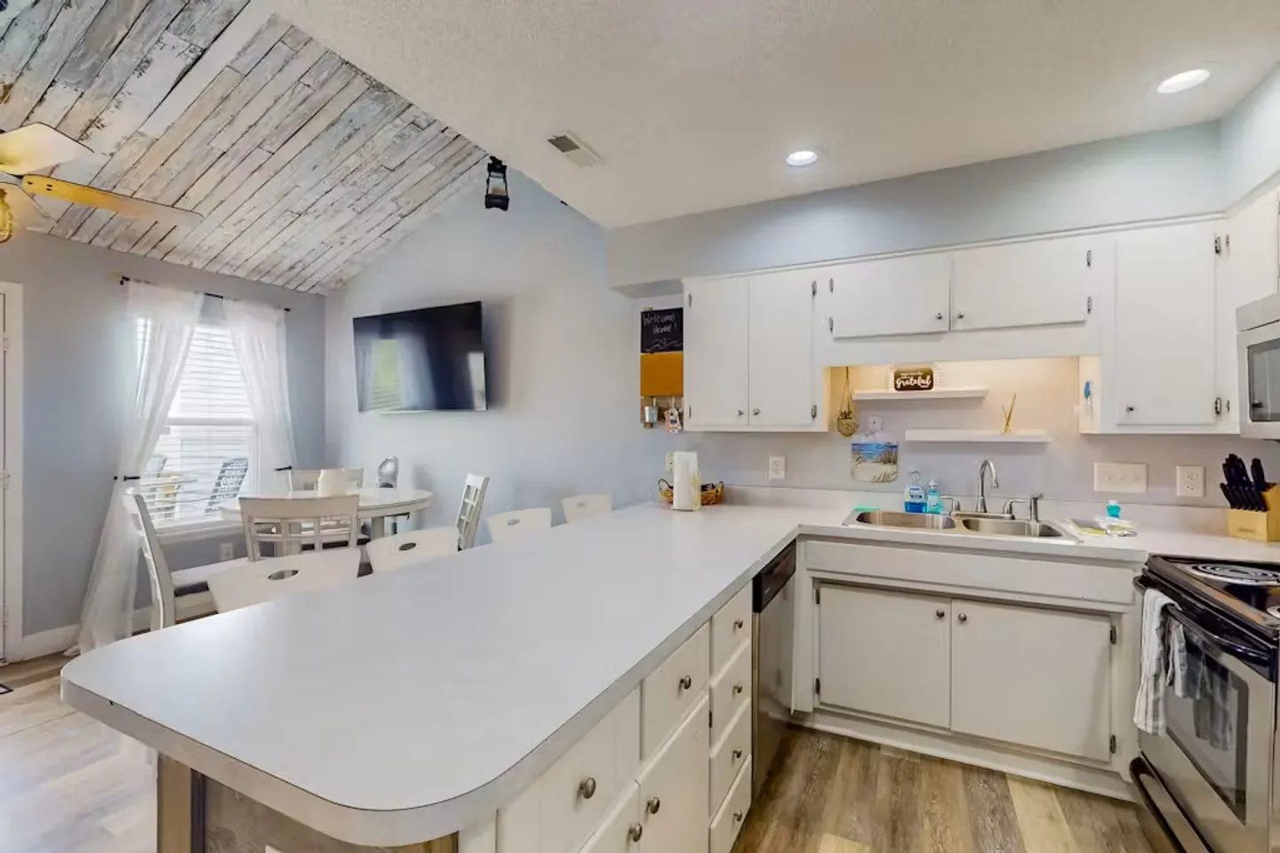 Kitchen with white cabinetry, peninsula counter, and adjoining dining area with a wood-plank ceiling accent.