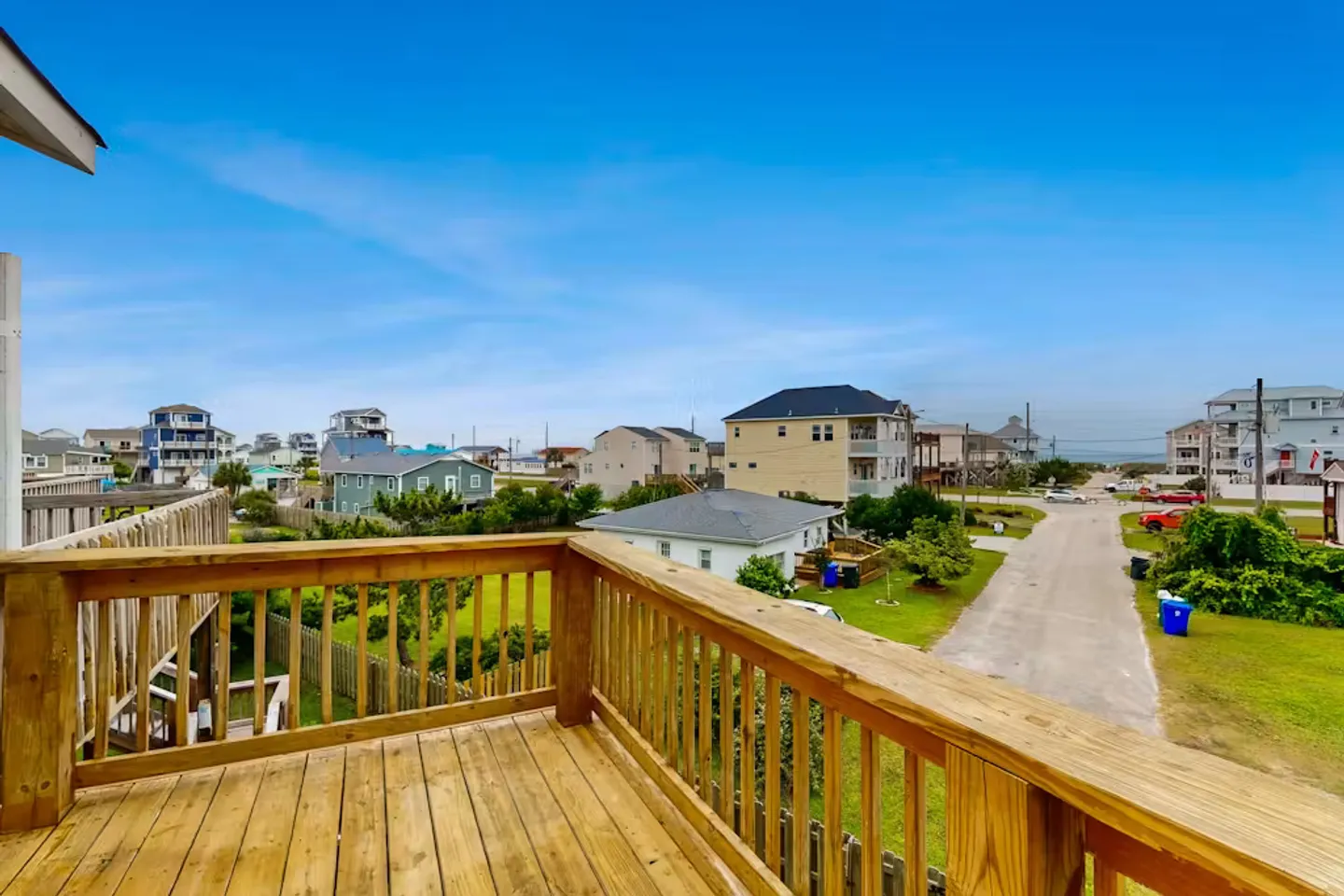 Elevated wooden deck overlooking a coastal neighborhood street with distant ocean views under a blue sky.