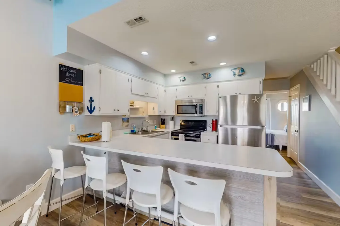 Open kitchen featuring a breakfast bar with four white barstools, white cabinetry, and stainless steel appliances.