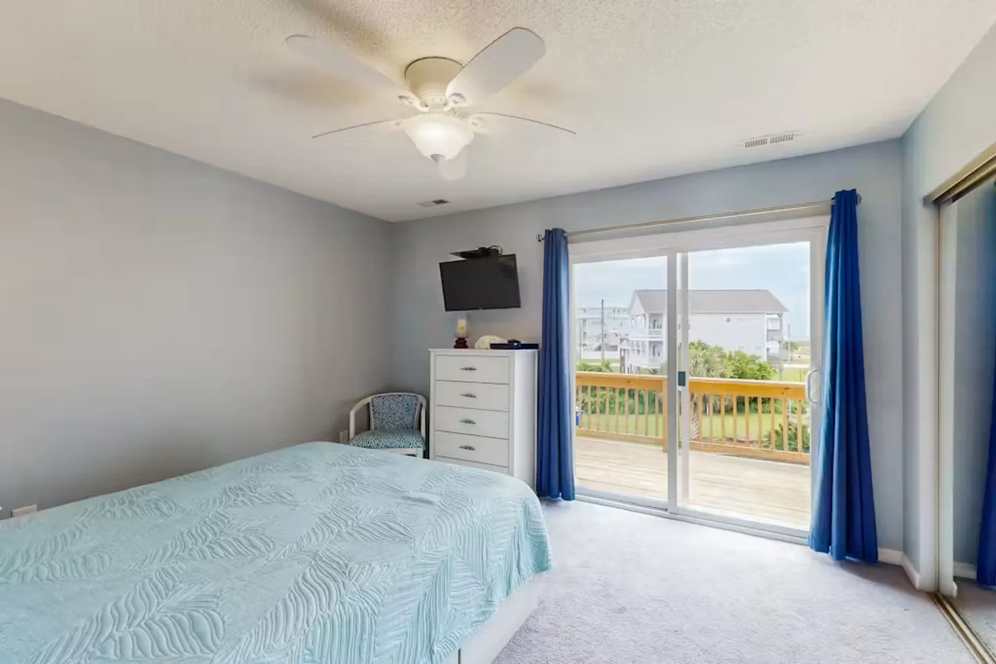 Bedroom with a bed, light blue walls, ceiling fan, and sliding glass doors leading to an outdoor deck.