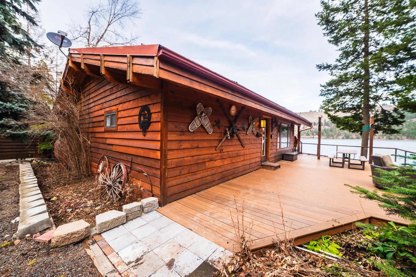 Exterior of a wood-sided cabin with a spacious deck overlooking a body of water.