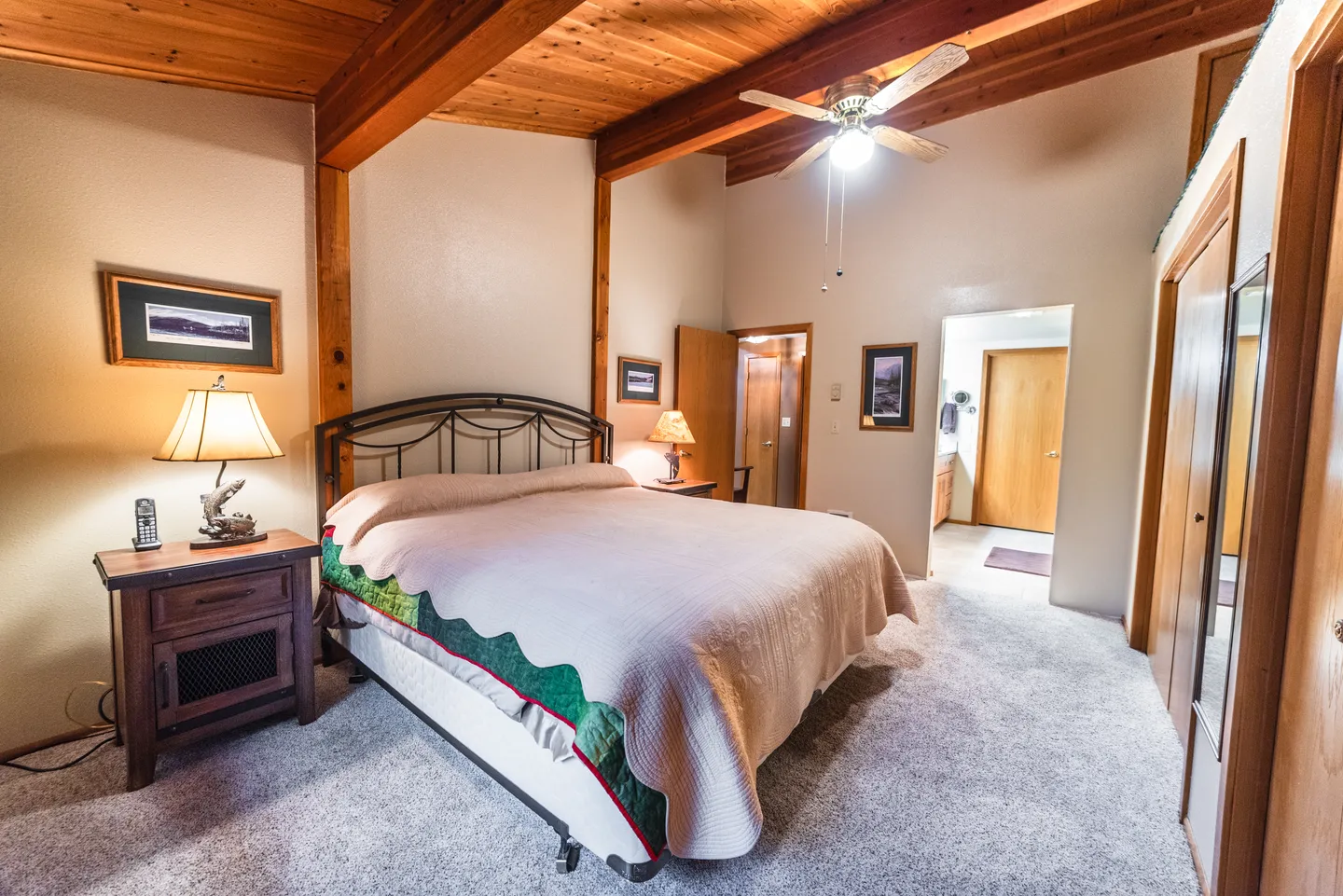 Bedroom with vaulted wood-beamed ceiling, metal frame bed, carpet, and an adjacent bathroom.