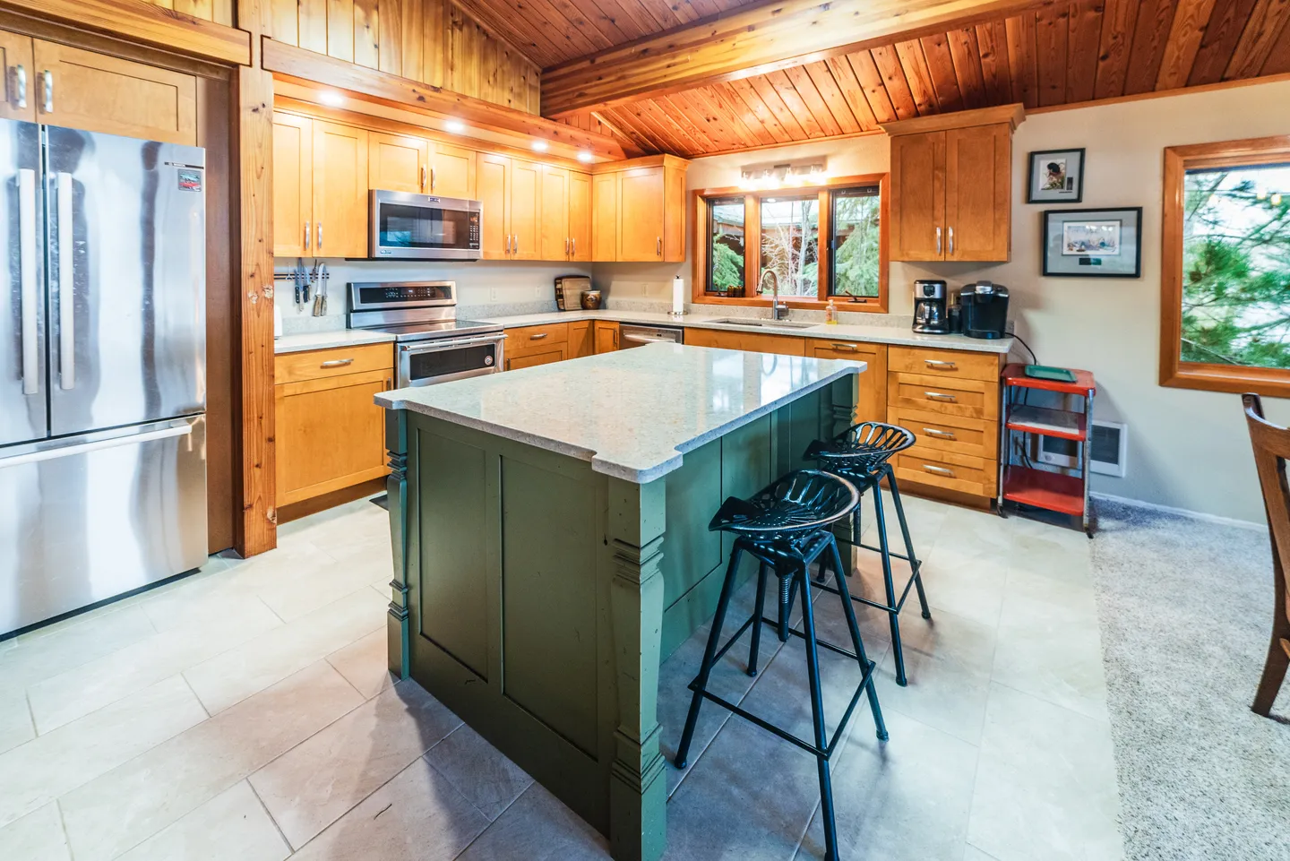 Kitchen with wood cabinetry, wood-paneled ceiling, stainless steel appliances, and a green kitchen island with barstools.