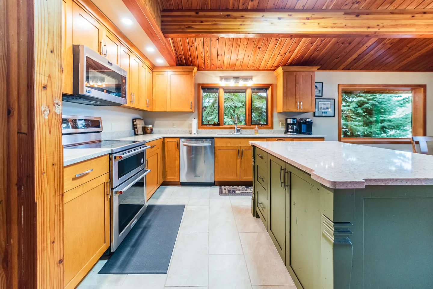 Kitchen with wooden cabinetry, stainless steel appliances, a wood-paneled ceiling, and a large green island with light countertops.