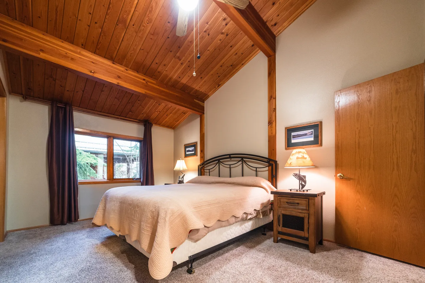 Bedroom with vaulted wood-paneled ceiling, exposed beam, carpeted floor, and made bed with nightstands.