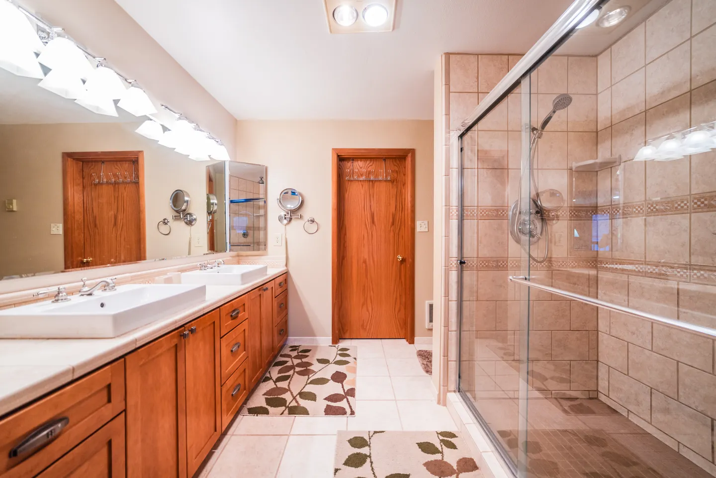 Bathroom featuring a double-sink wood vanity with a large mirror and a walk-in shower with sliding glass doors.