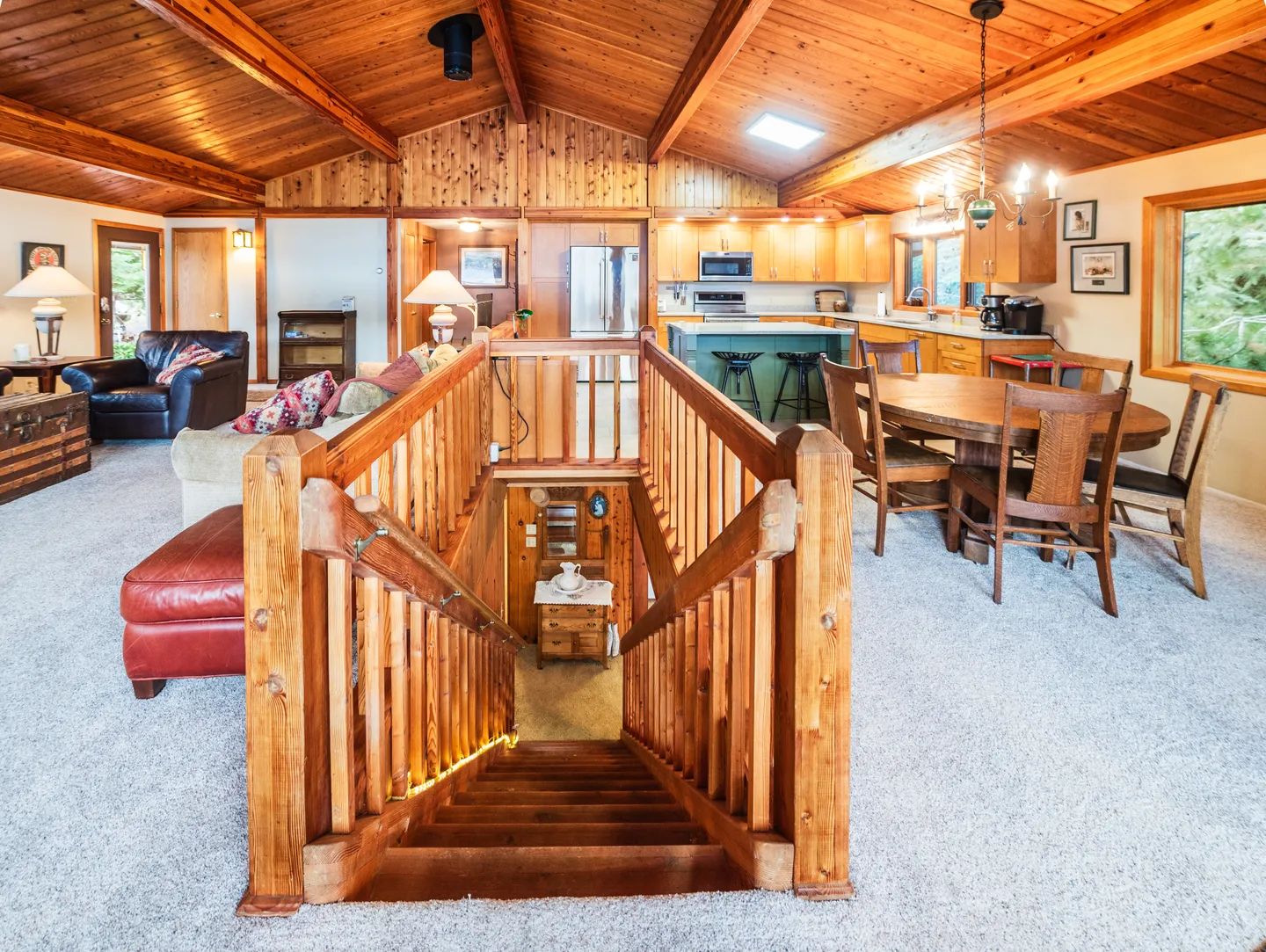 Elevated view looking down a central wooden staircase in an open-concept living, dining, and kitchen space with wood-paneled vaulted ceilings.