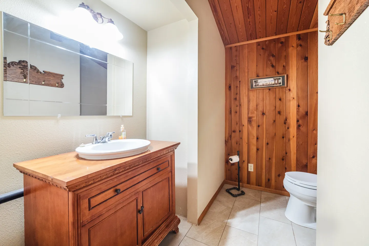Bathroom with wooden vanity, oval sink, large mirror, tile floor, and a toilet next to a wood-paneled accent wall.