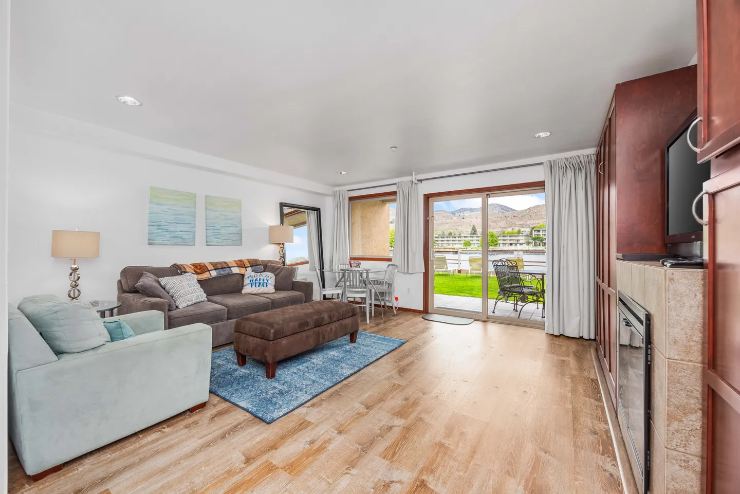 Living room with sofa, armchair, fireplace, and sliding glass doors opening to a patio and grassy area.