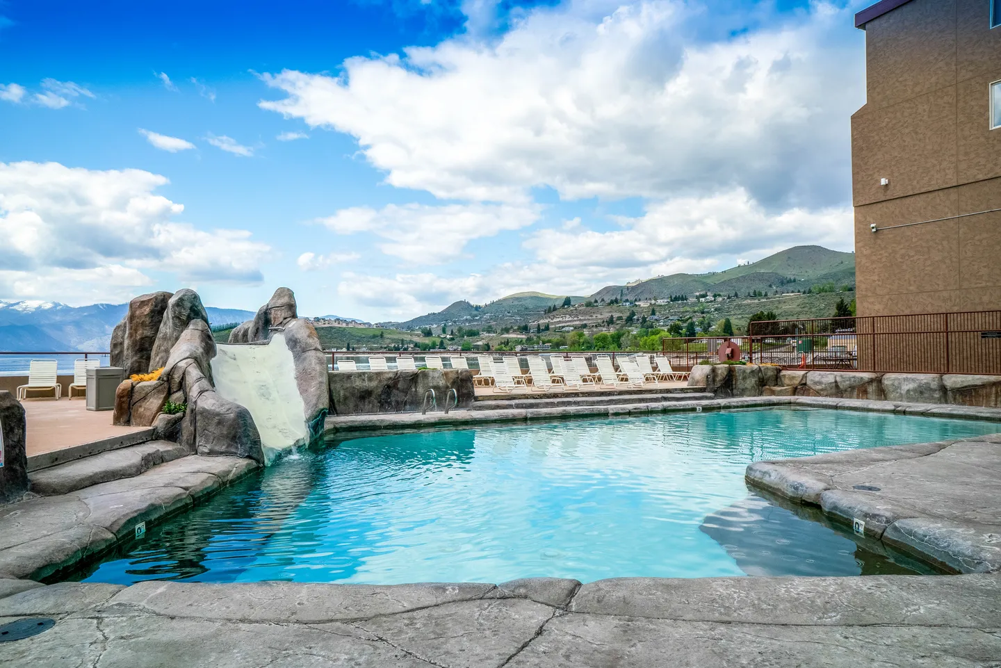 Outdoor swimming pool featuring a rock-style water slide and pool deck with mountain views.