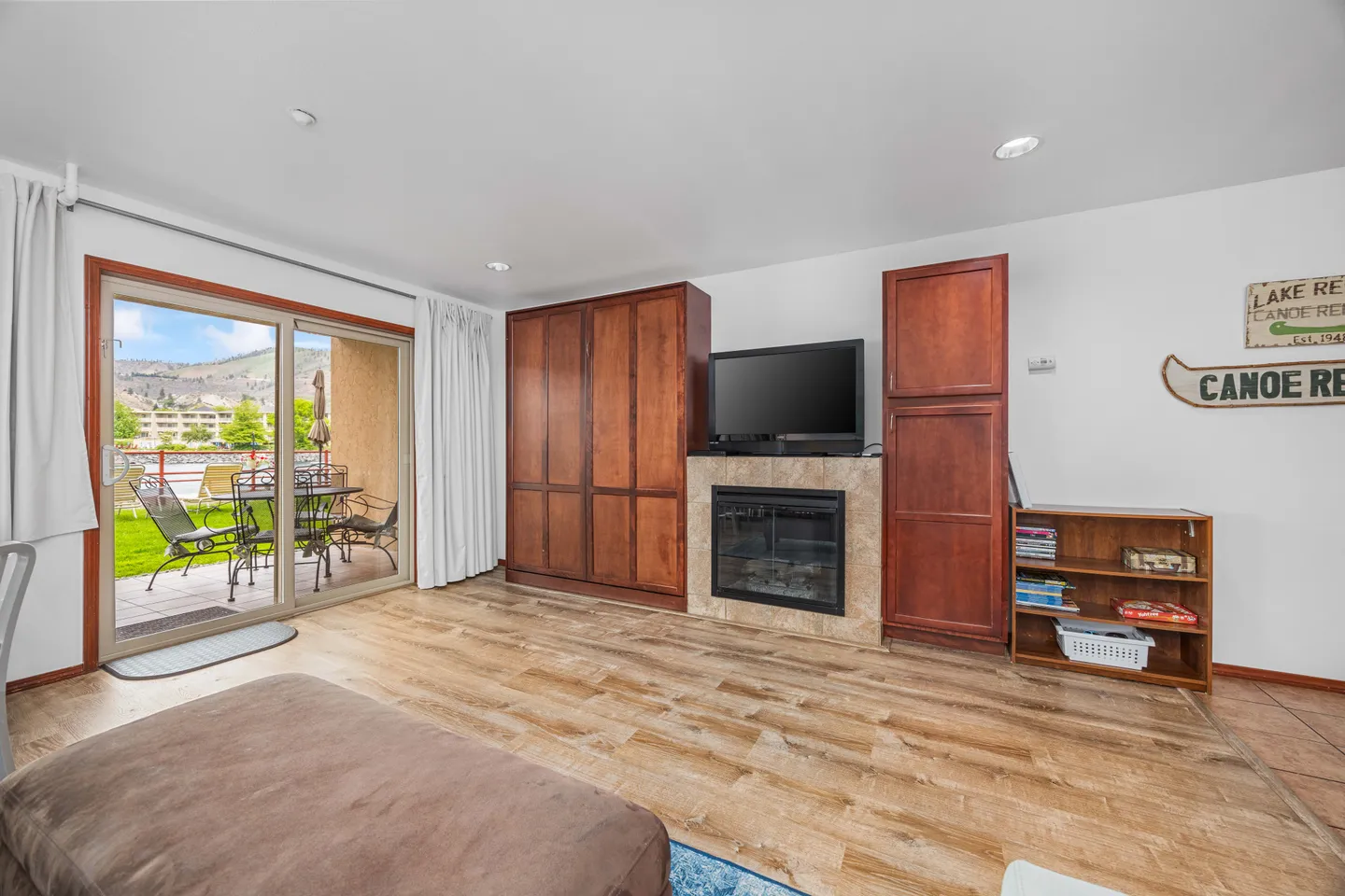 Living room with wood-style flooring, a fireplace flanked by wooden cabinets, a flat-screen TV, and sliding glass doors opening to an outdoor patio.