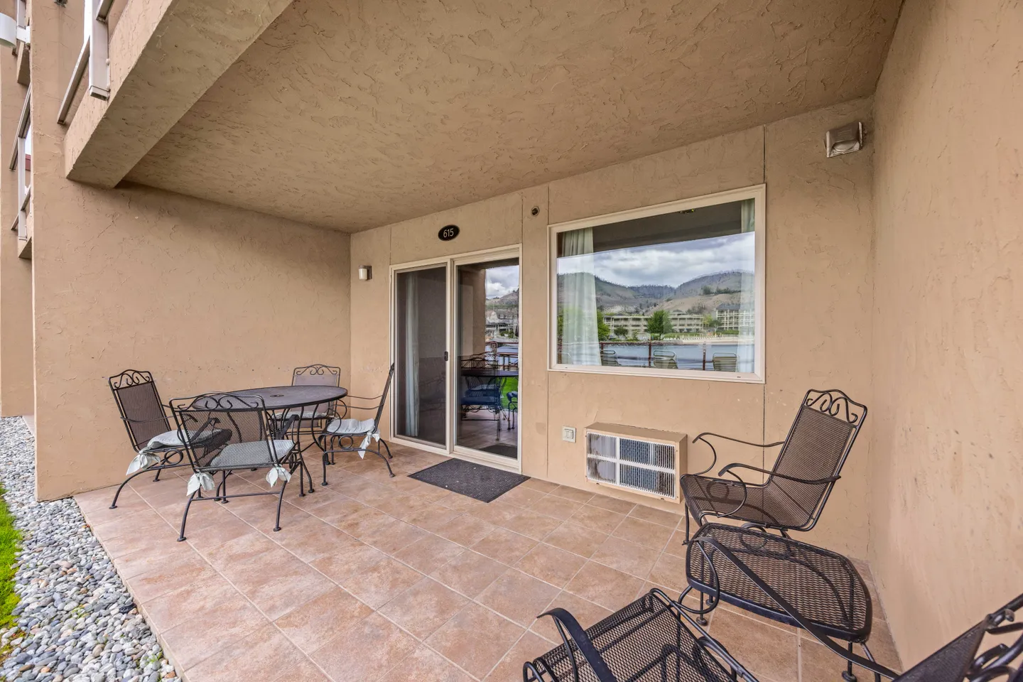 Tiled ground-floor patio with outdoor dining set, armchairs, and glass sliding door against a stucco wall.