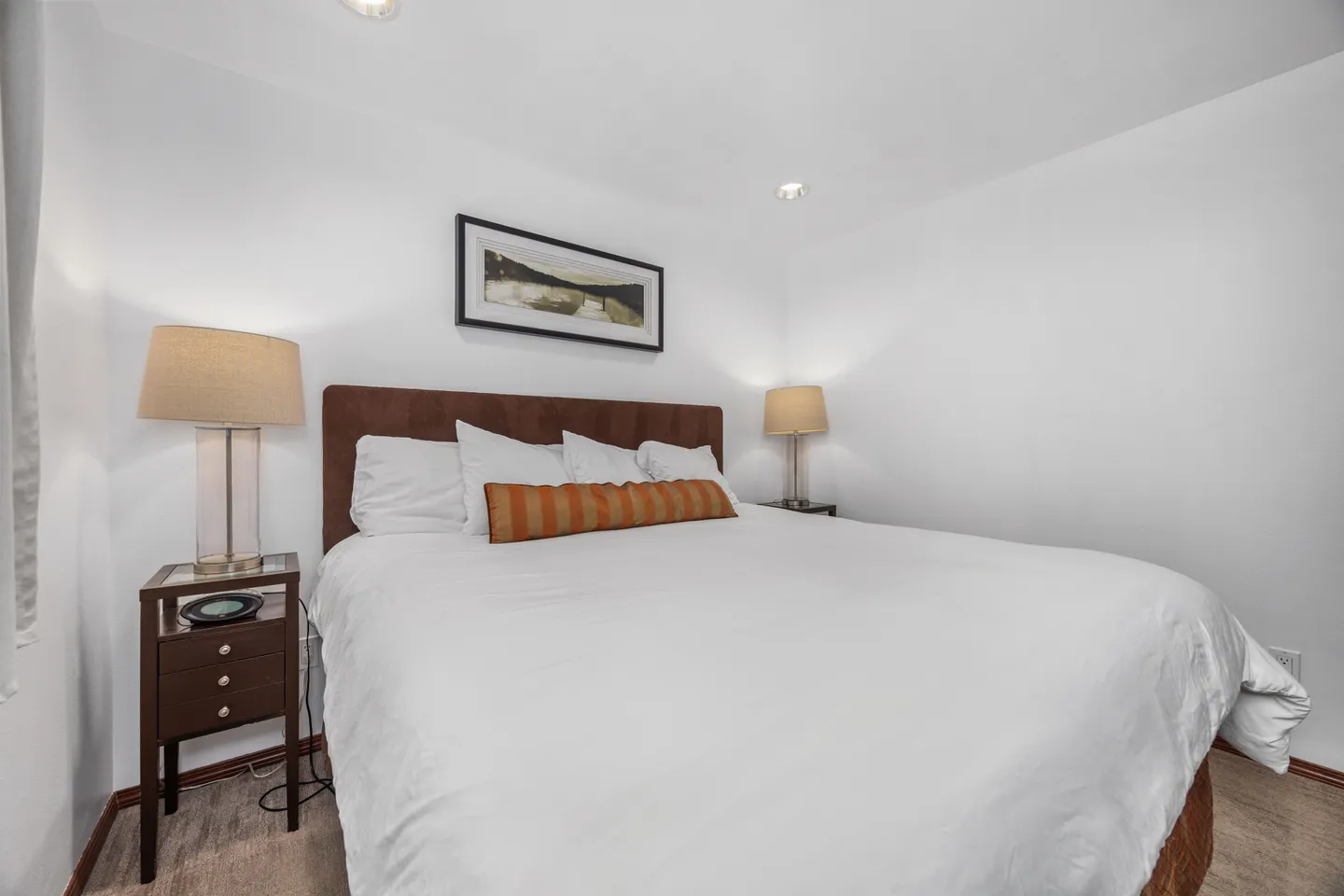 Bedroom with a large bed dressed in white linens, an upholstered headboard, and matching nightstands with lamps.