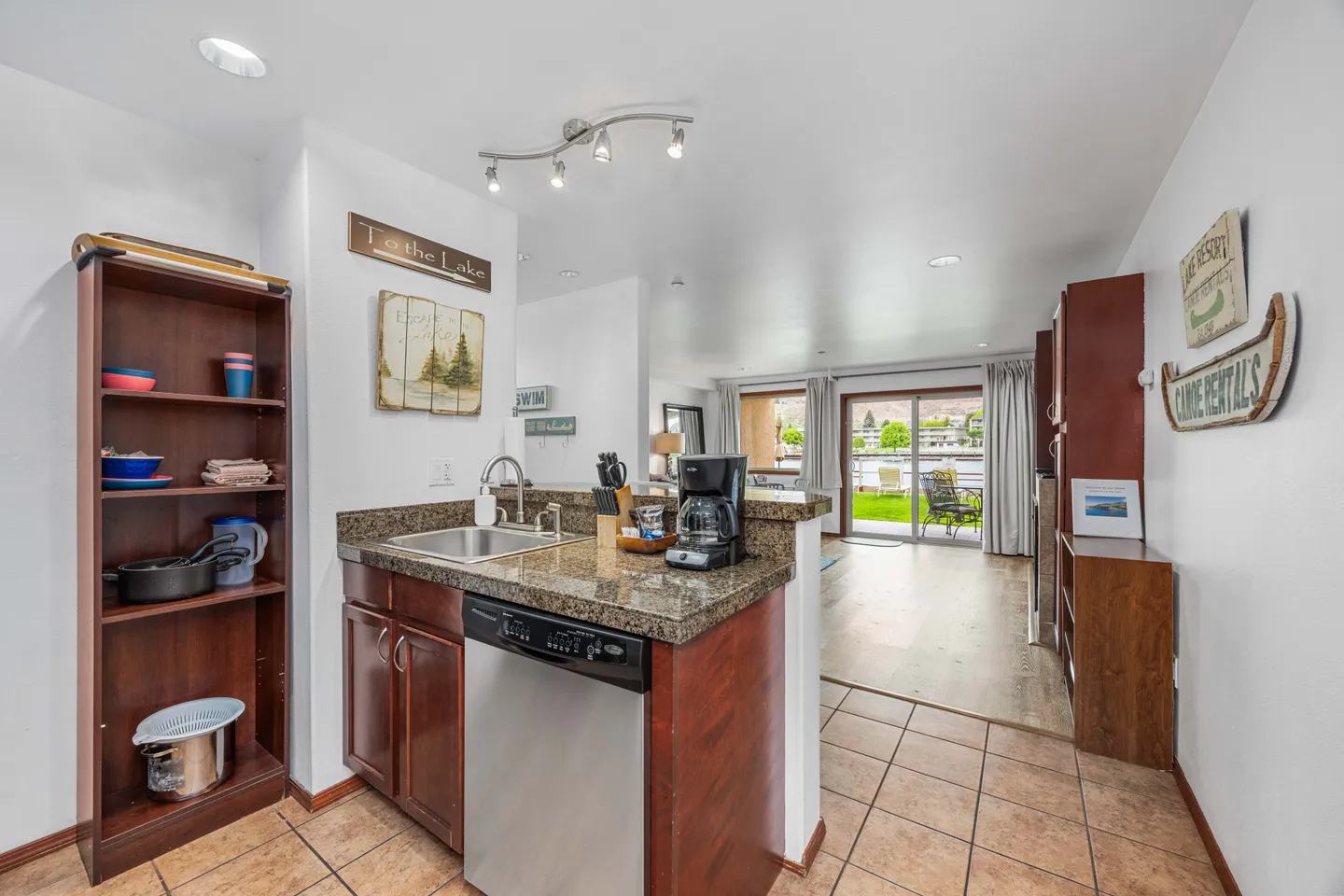 Kitchen counter with dishwasher and sink opening to a living area with sliding glass doors leading outside.