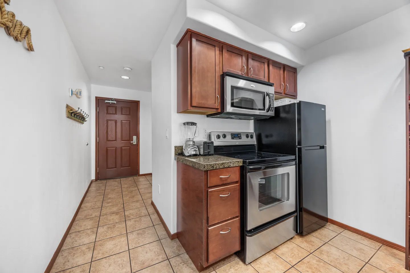Kitchen area with wood cabinetry, stainless steel oven, built-in microwave, and refrigerator next to an entry hallway.