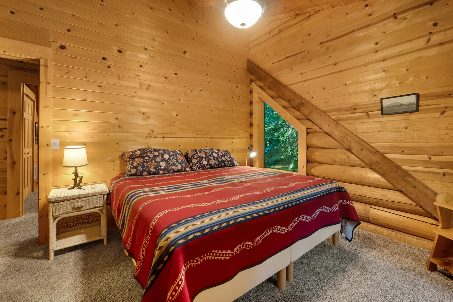 Bedroom with log siding, wood-paneled walls, carpet, and a bed dressed with a patterned red blanket.