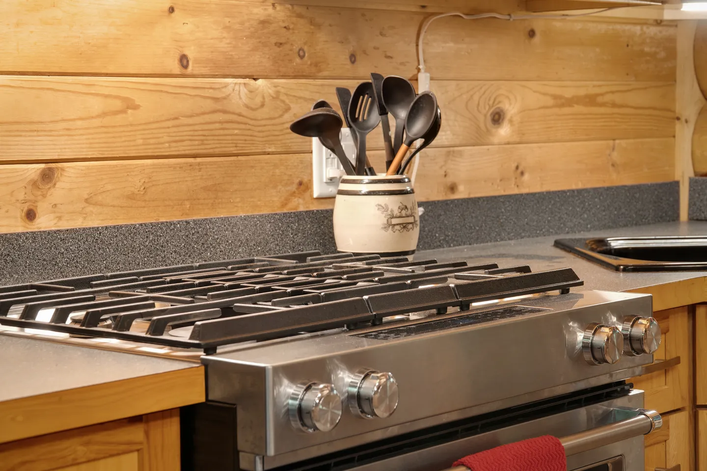 Close-up of a stainless steel gas range and cooktop in a kitchen with wood-paneled walls.