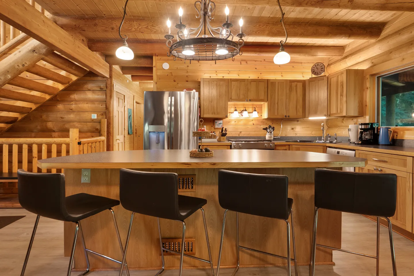Kitchen in a log home with wood cabinetry, a kitchen island with four barstools, and a log staircase on the left.