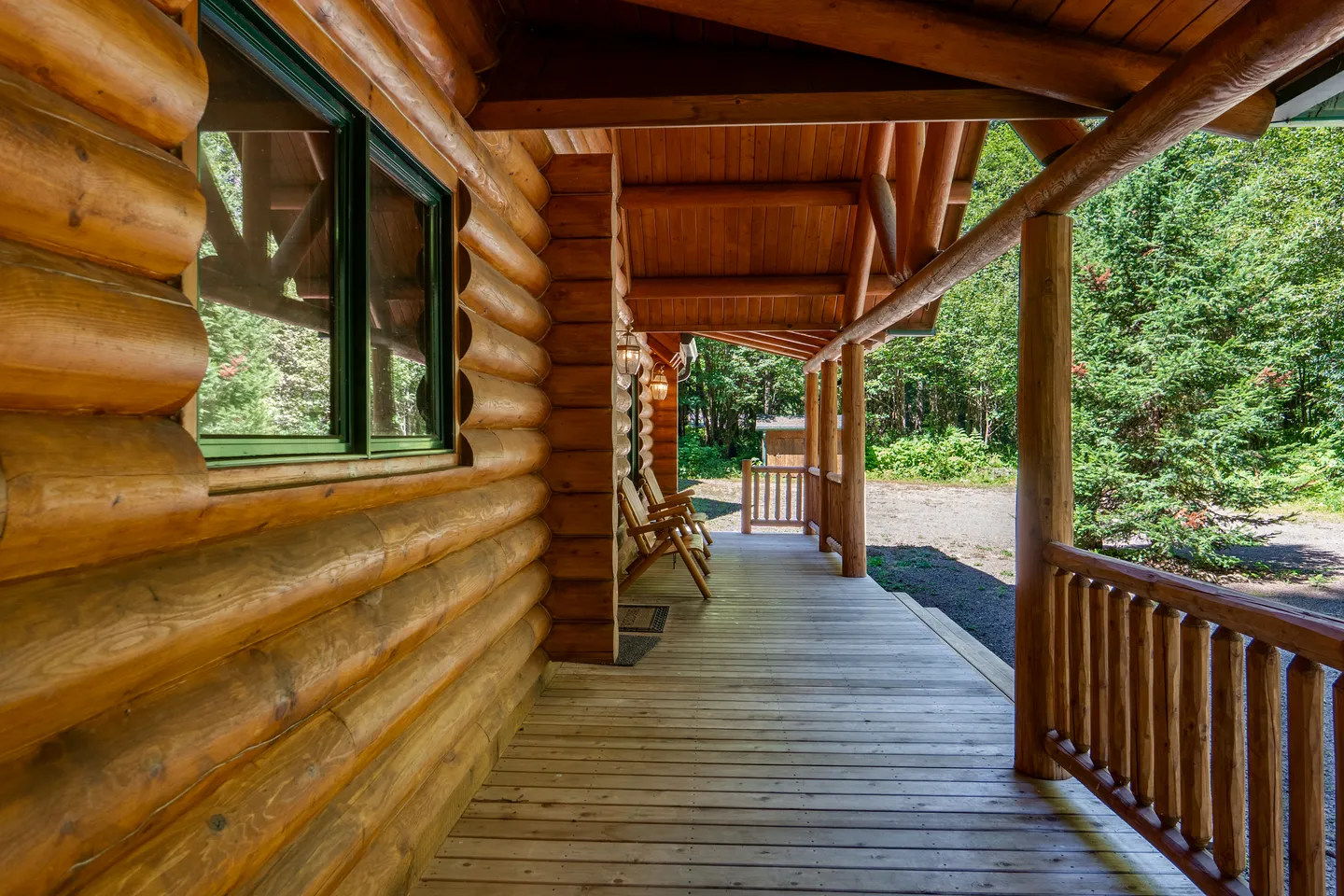 A covered wooden porch along the exterior of a log cabin with outdoor seating.