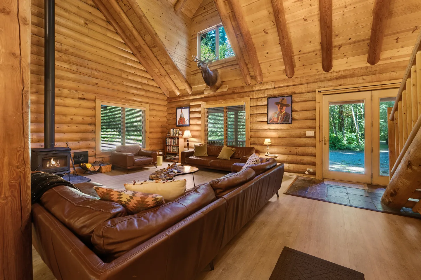Living room with log walls, vaulted wood ceiling, leather sectional sofa, and a wood stove.