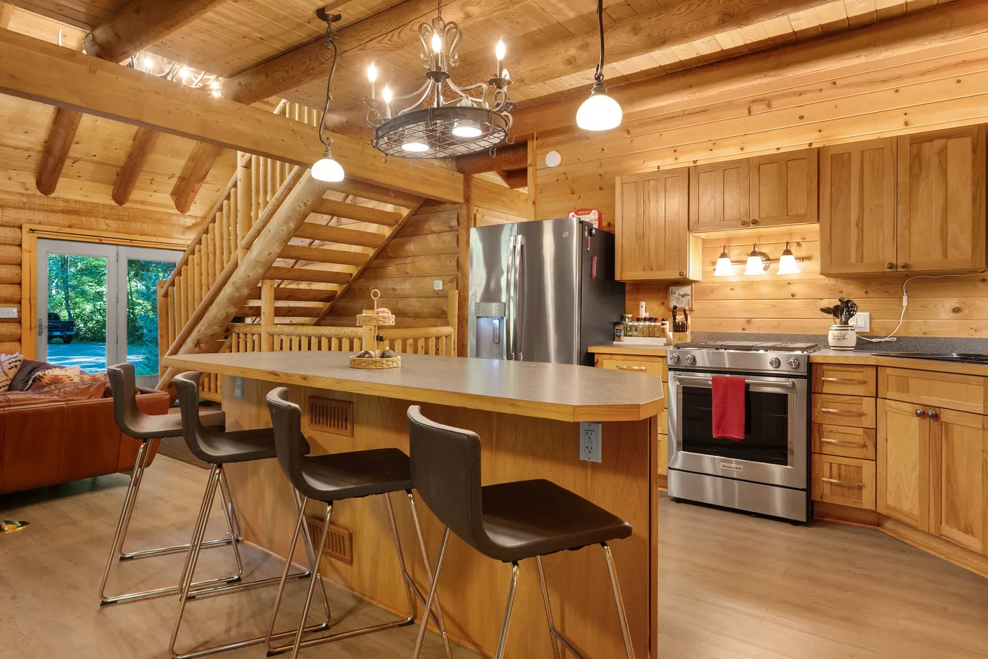Kitchen island with barstools in a log cabin home featuring stainless steel appliances and an open wooden staircase.