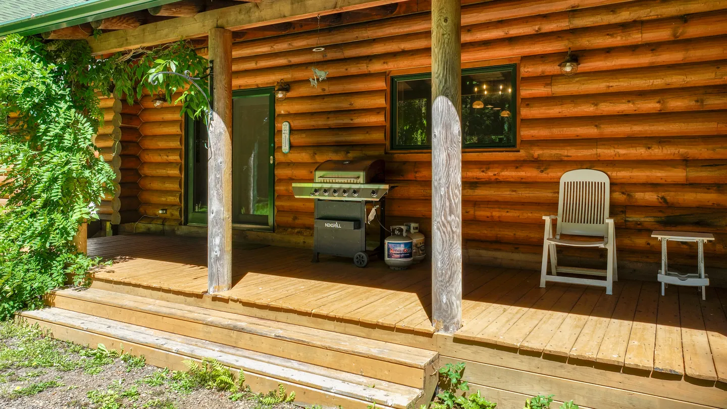Covered wooden porch of a log cabin with a gas grill, outdoor chair, and side table.