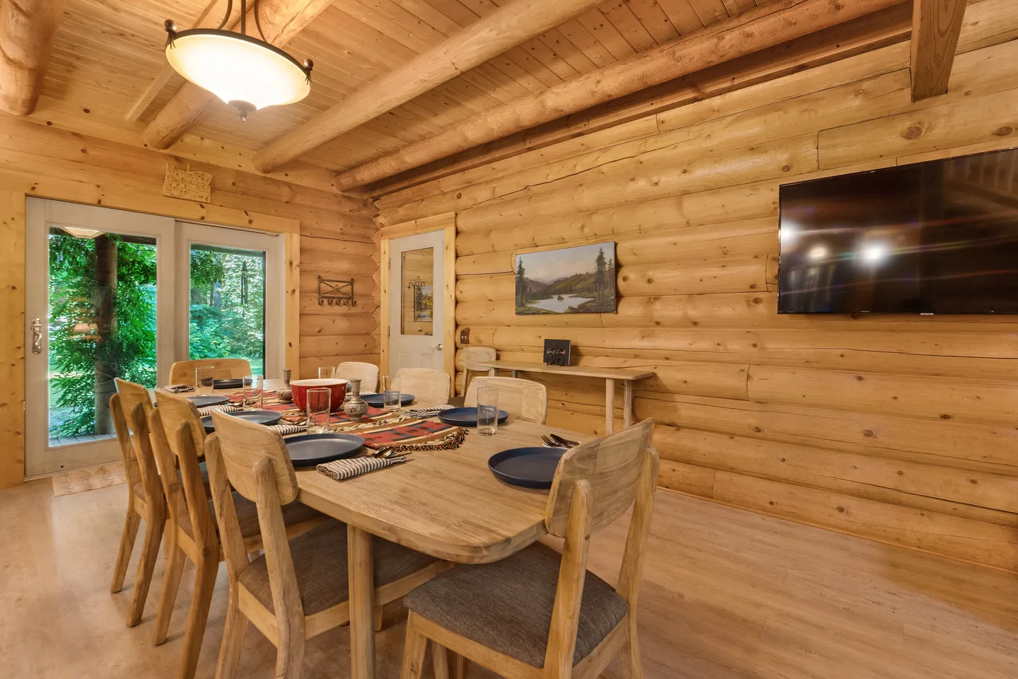 Dining area with a large wooden table, log walls, and a beamed wood ceiling.