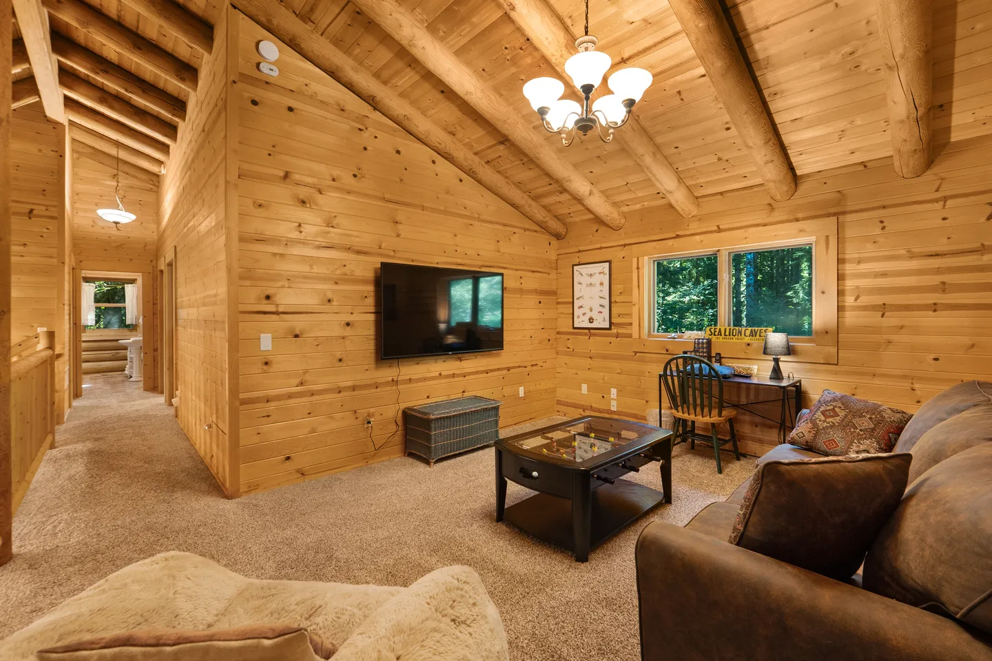A living area with wood-paneled walls, exposed log ceiling beams, a wall-mounted TV, coffee table, and sofa.