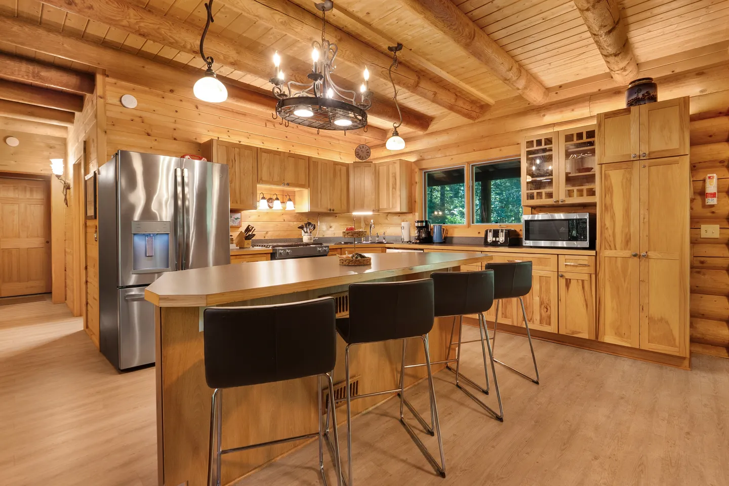 Kitchen in a log-style home with light wooden cabinetry, stainless steel refrigerator, and a central island with barstools.
