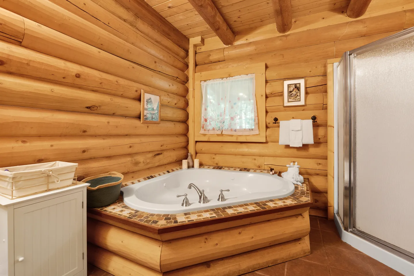 A corner jetted soaking tub with a tiled surround in a log cabin bathroom beside a glass-door shower.
