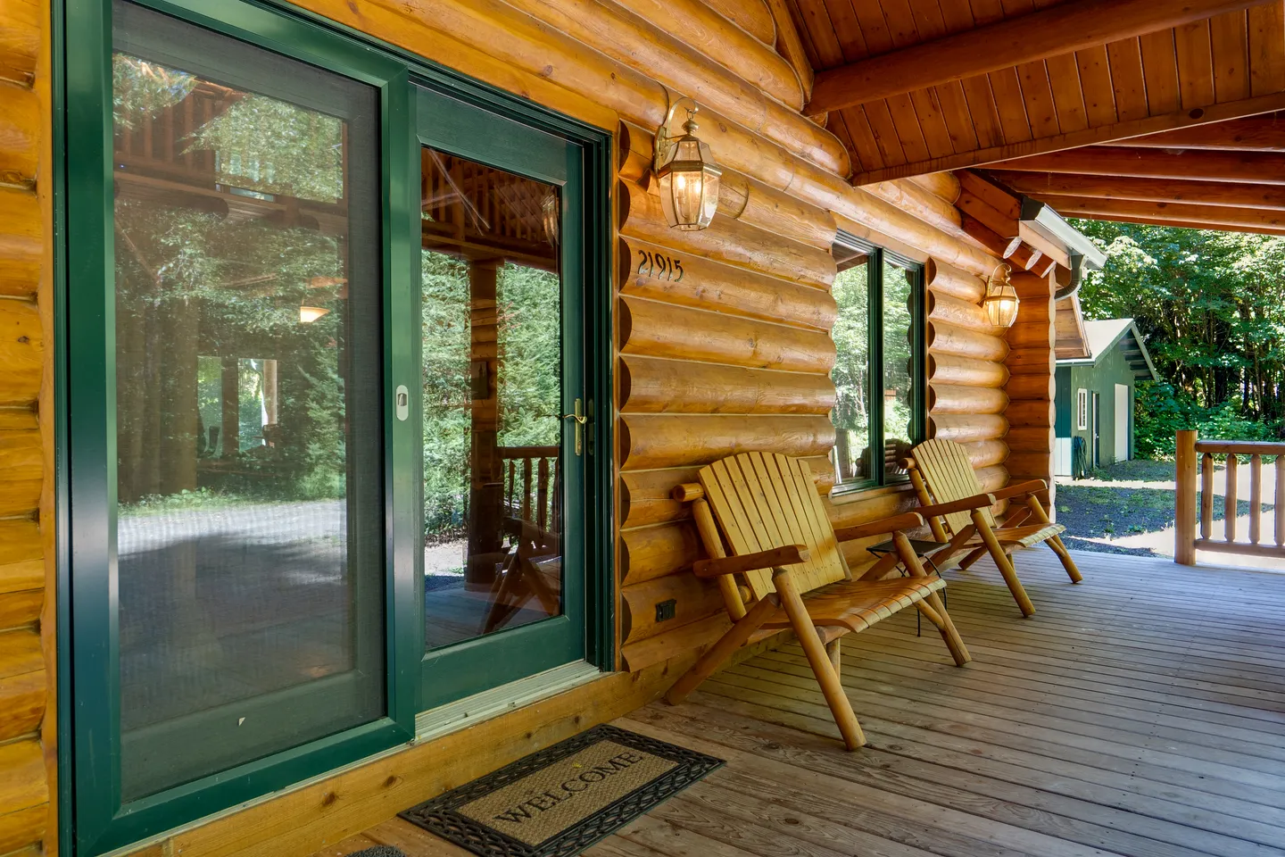 Covered wooden porch of a log cabin with outdoor seating and sliding glass entrance doors.