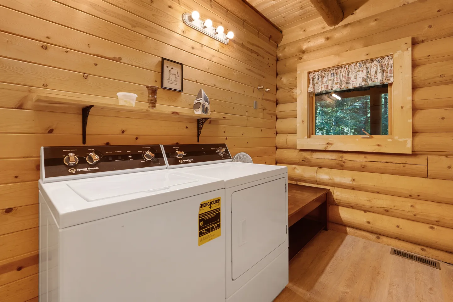 A laundry room inside a log cabin with a white washer and dryer, wood plank walls, and a small window.