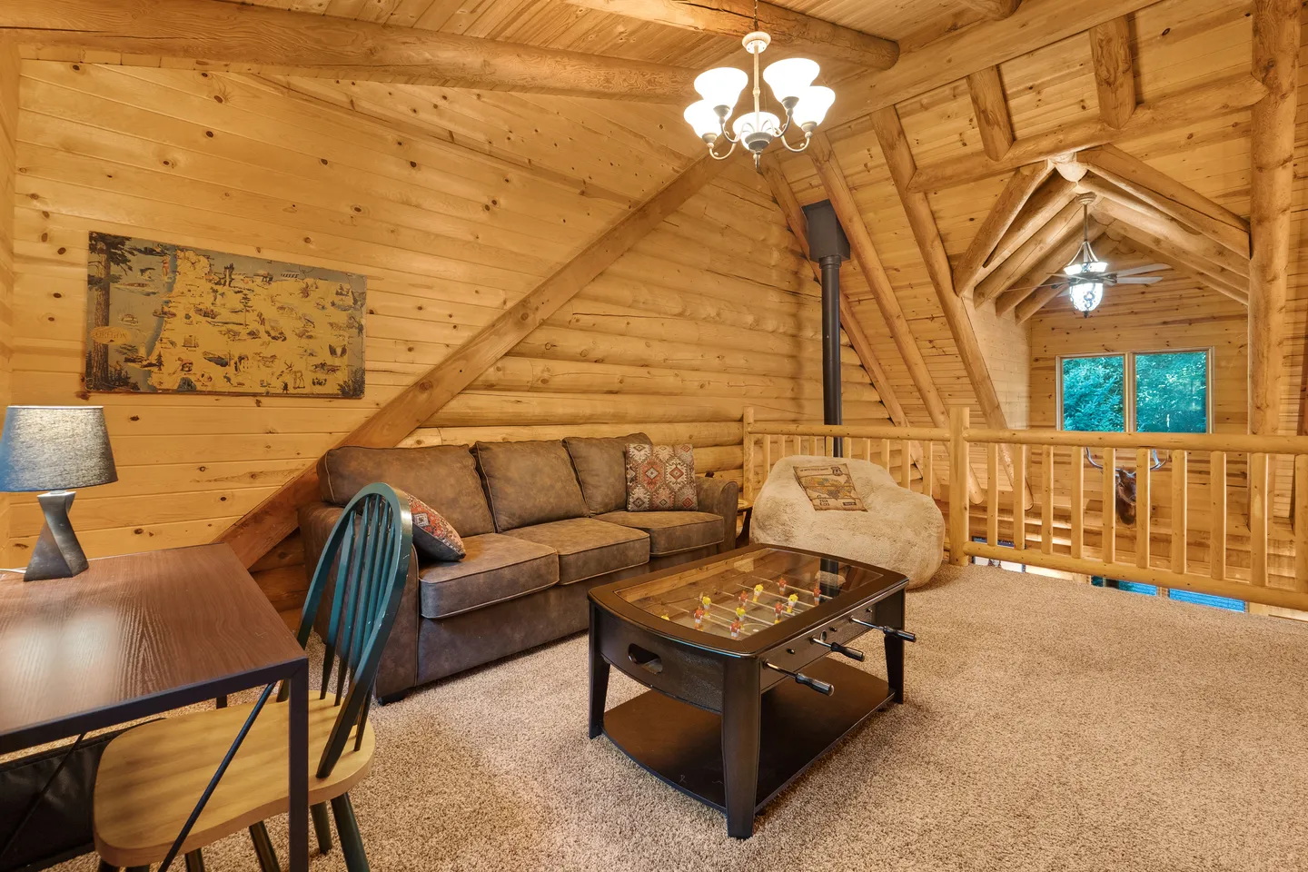 A cozy loft sitting area with log walls and ceiling, featuring a brown sofa, a foosball coffee table, and carpeted floors.