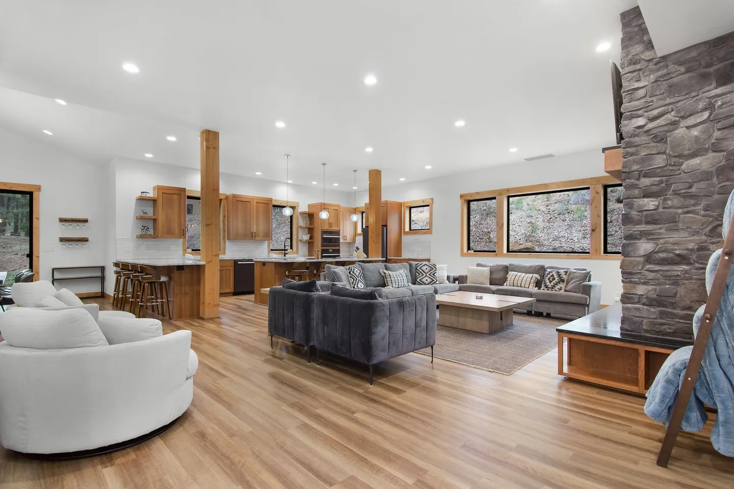 Open-concept living room and kitchen featuring wood-look floors, a stone fireplace, and ample seating.