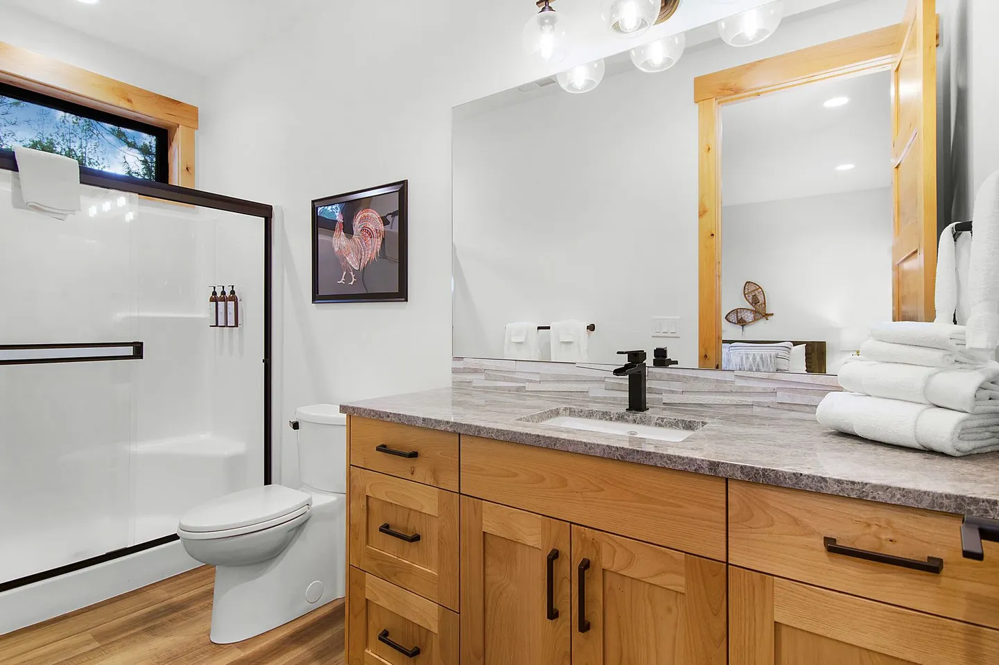 Bathroom featuring a light wood vanity with a dark faucet, large mirror, toilet, and walk-in shower with sliding glass doors.
