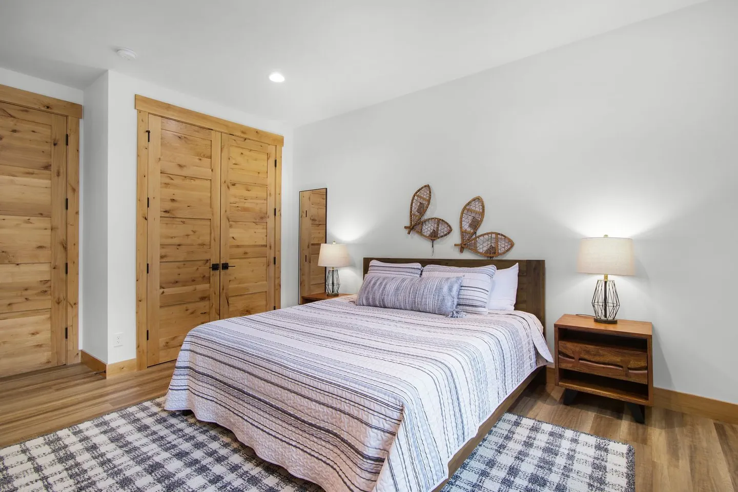 Bedroom featuring a made bed with striped bedding, rustic wood closet doors, and snowshoe wall decor.
