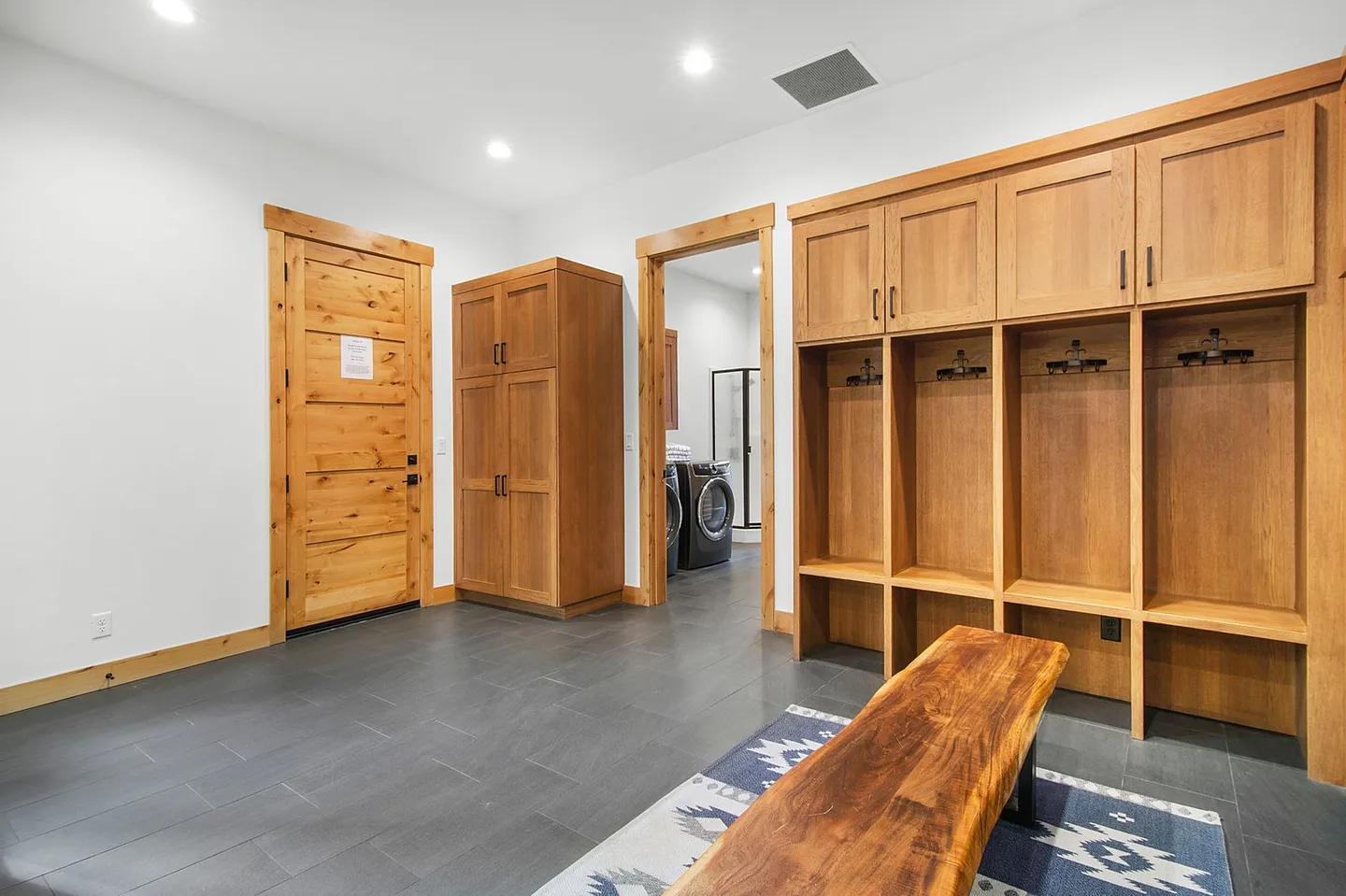 Mudroom with tiled floor, wooden bench, built-in wooden storage lockers, and a doorway leading to a laundry room.