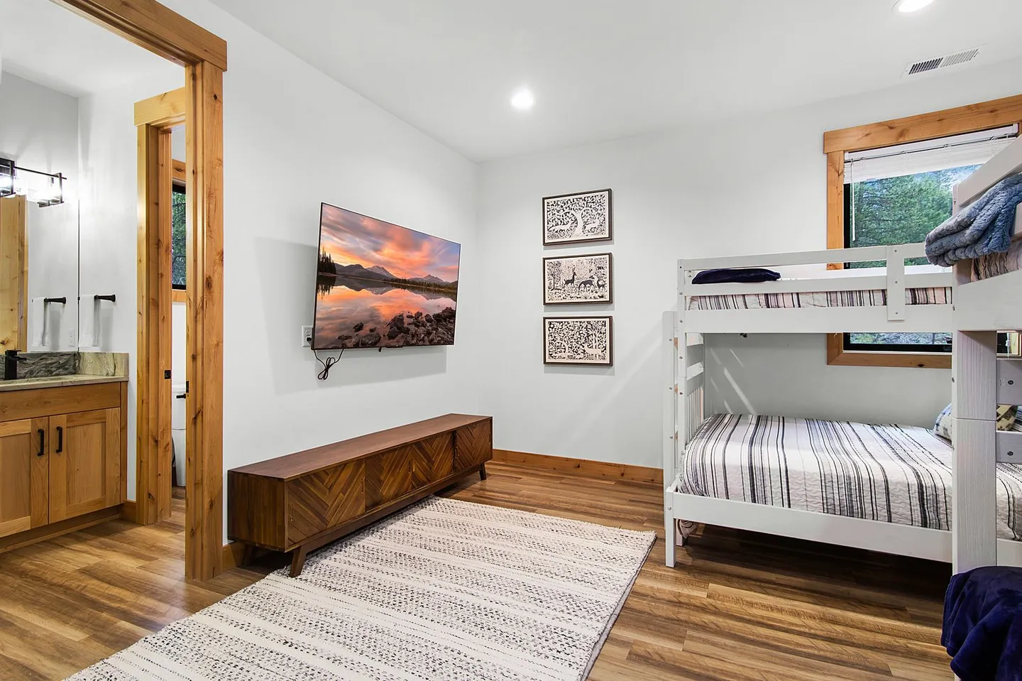 Bedroom with a white wooden bunk bed, a wall-mounted TV over a low credenza, and an open doorway leading to a private bathroom.