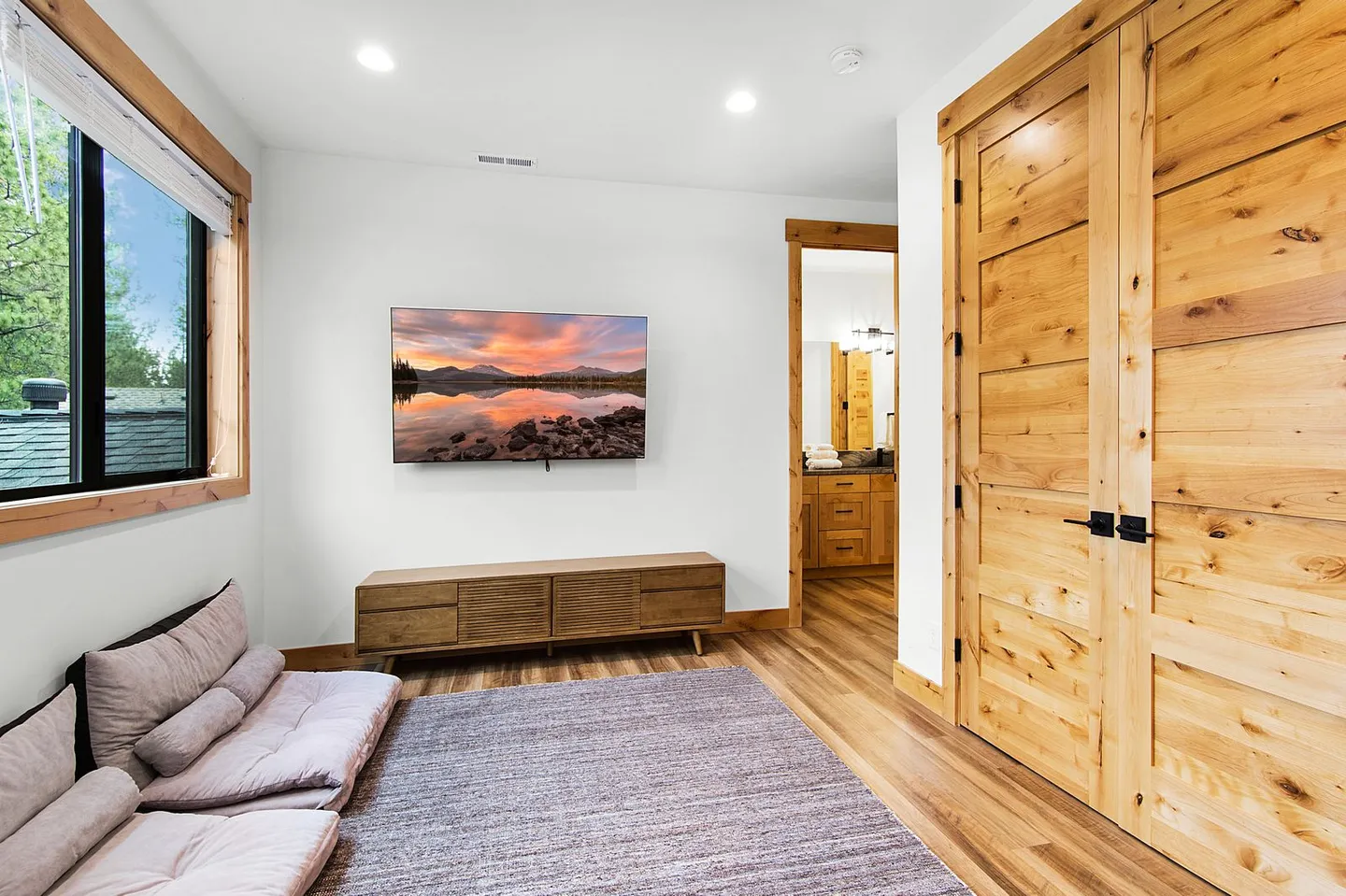Living area with floor seating, a large wall-mounted television, a wood media console, and a large wooden sliding door.