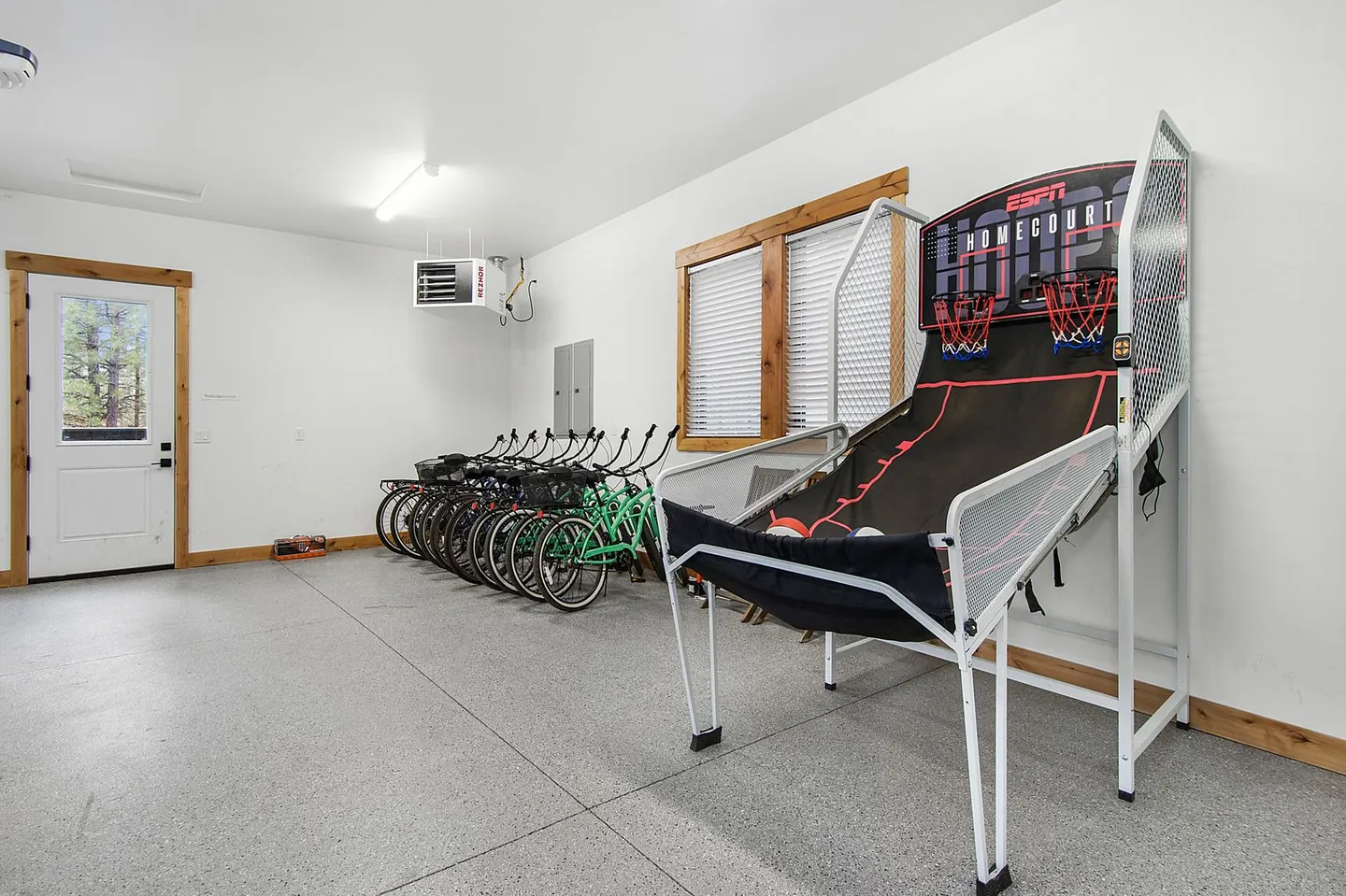 Garage converted into a recreation area with an arcade basketball game, several bicycles parked along the wall, and an exterior door.