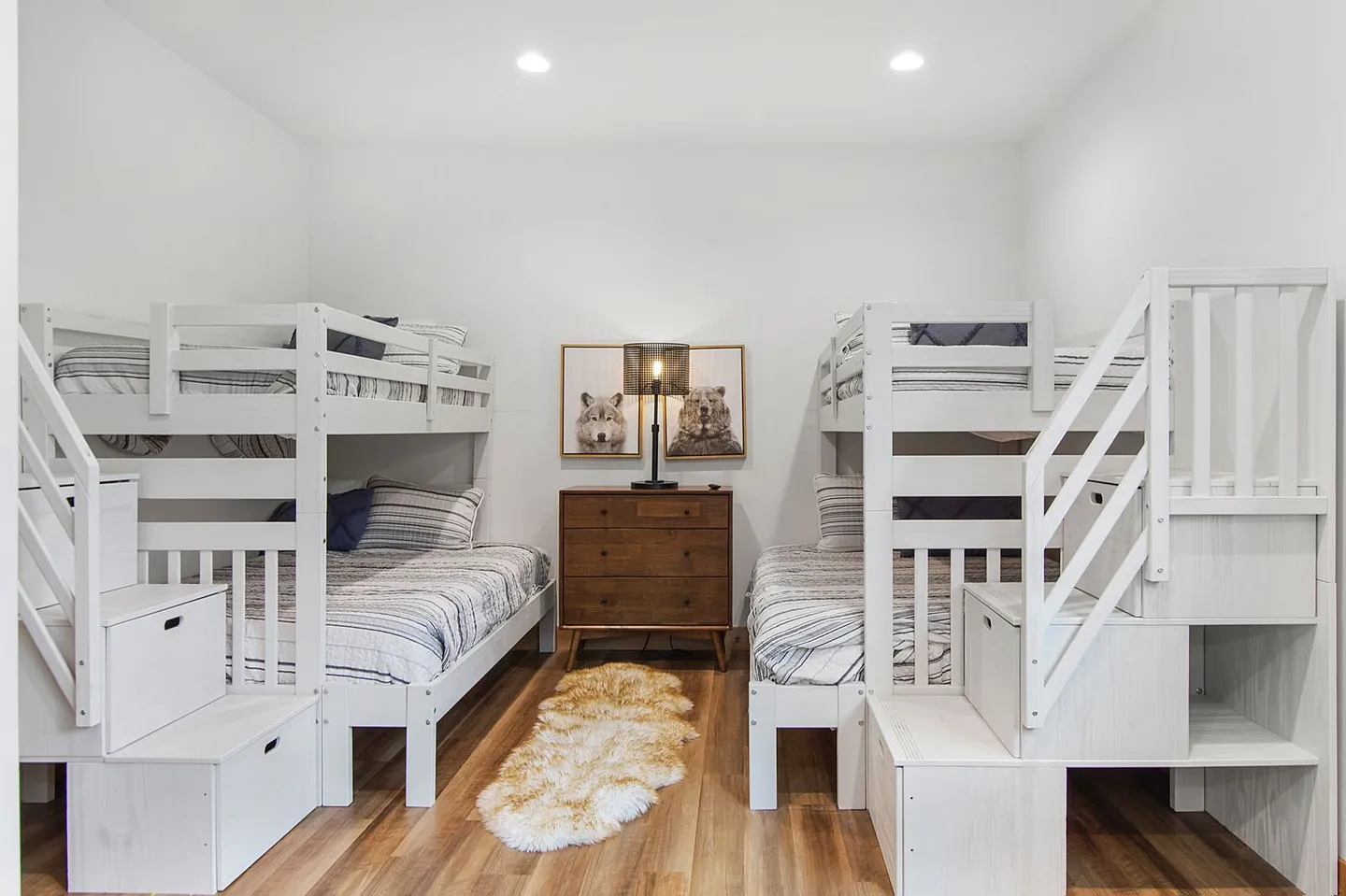 Bunk room featuring two sets of white wooden bunk beds with built-in storage steps flanking a wooden dresser.