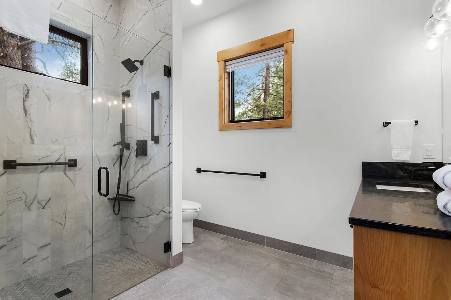 Bathroom with a glass-enclosed walk-in shower featuring marble-patterned tile, matte black fixtures, a toilet, and a vanity.
