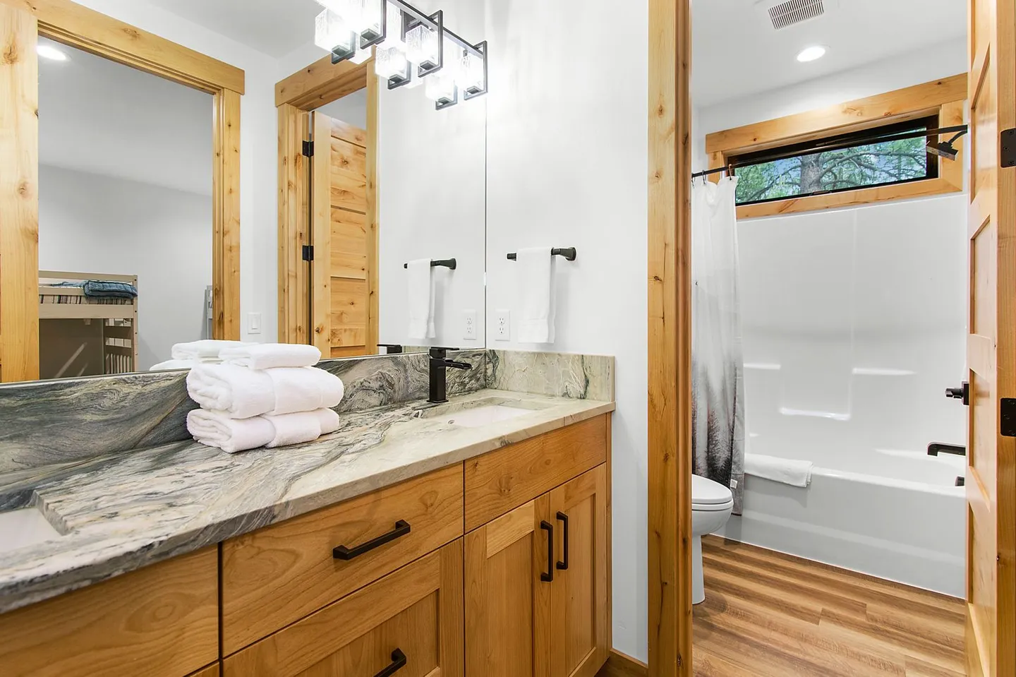 Bathroom with a double-sink stone vanity, wood cabinets, large mirror, and view into an adjacent shower and bathtub area.